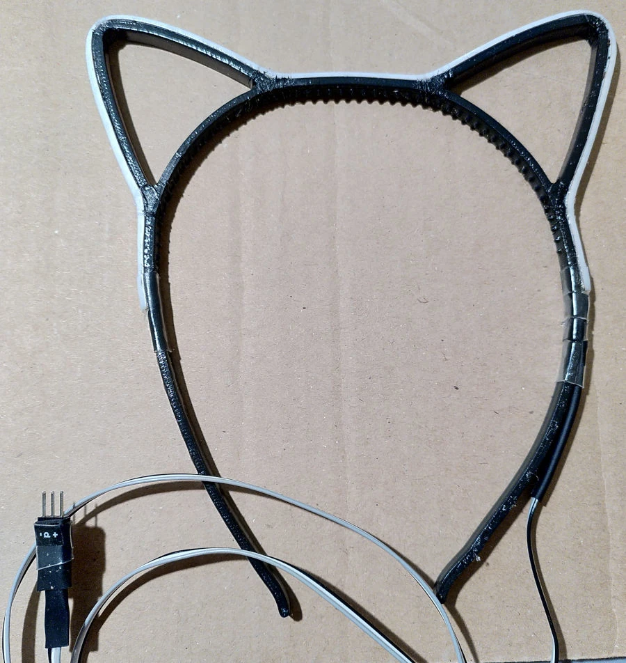 Catears with a powered off led strip glued to it. At the end of the cable coming from the catears is a plug with three exposed pins.